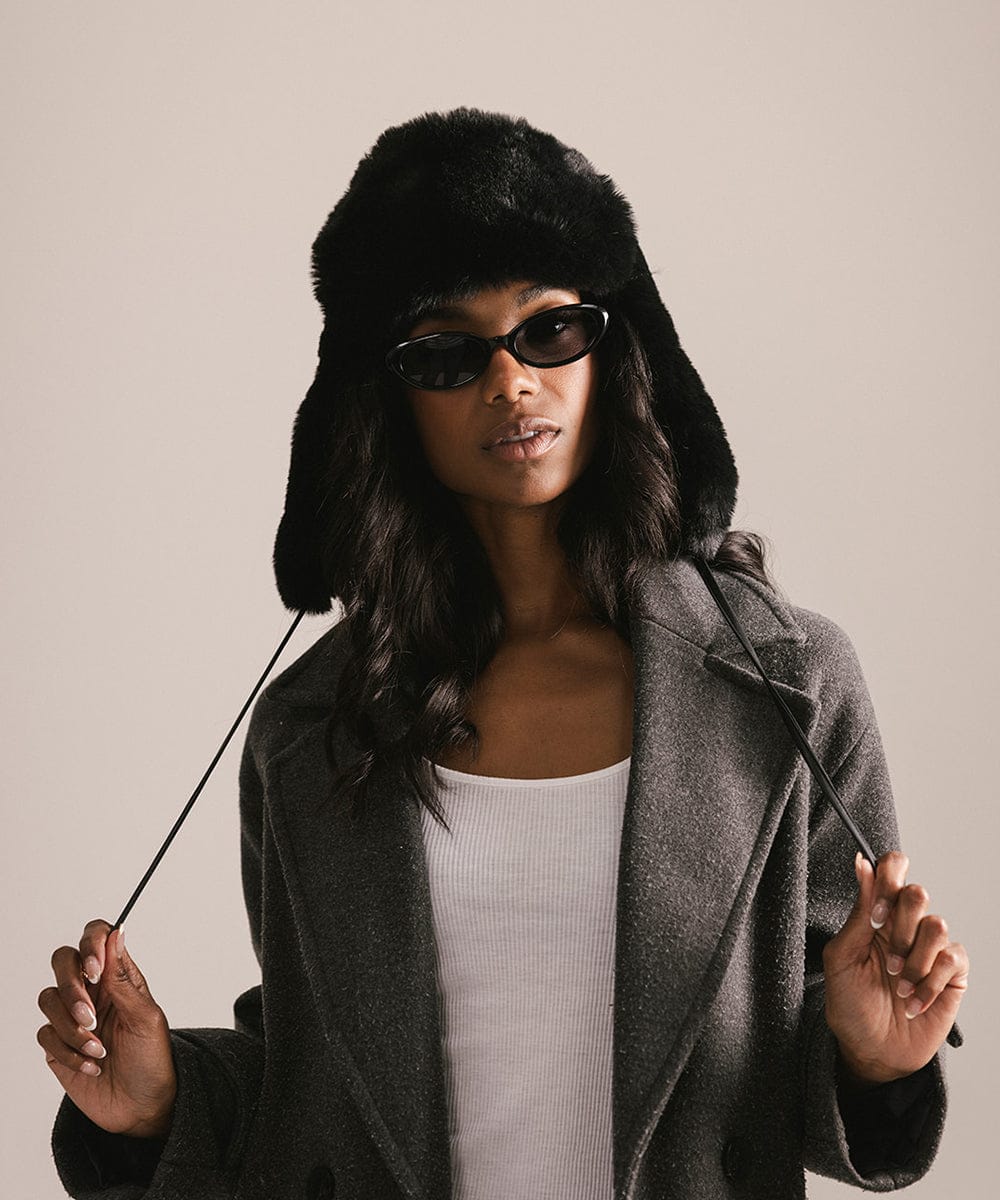 Woman wearing a black fur hat, sunglasses, and a gray coat against a plain background #color_black