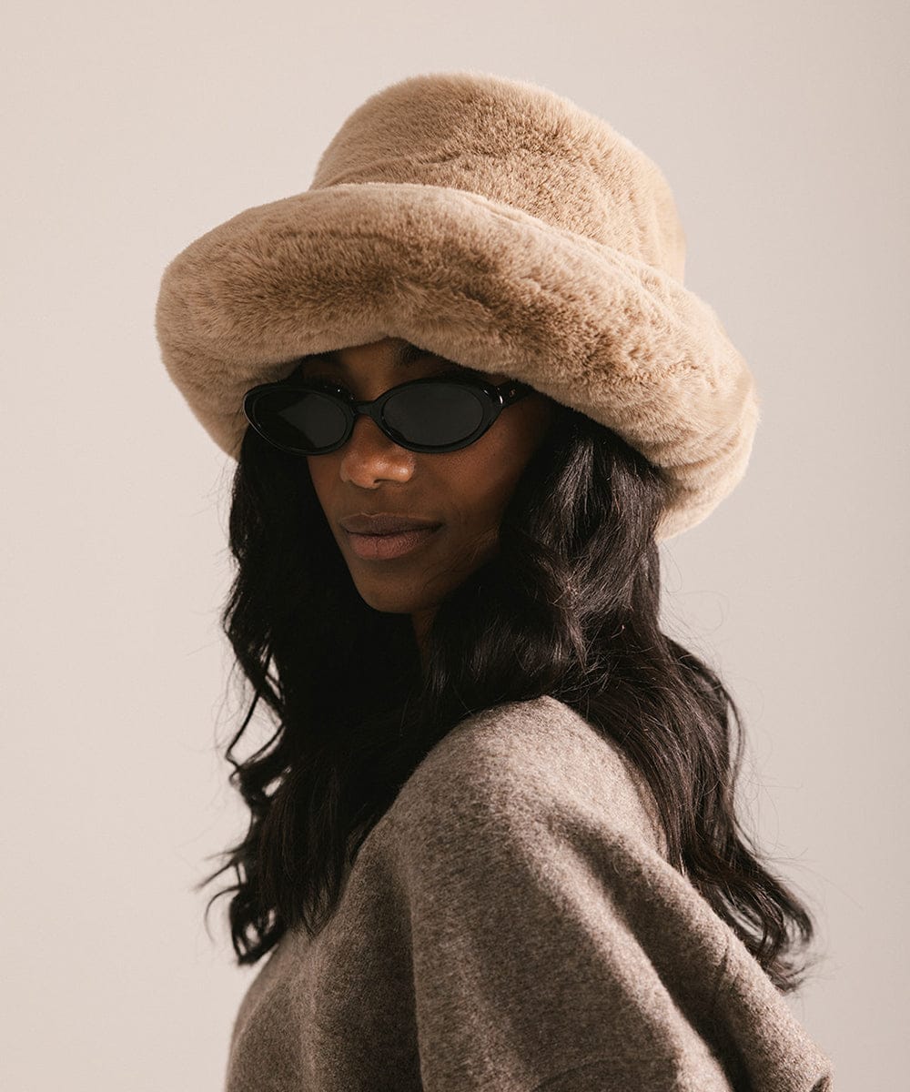 Woman wearing a beige fur hat and sunglasses with a neutral background #color_tan