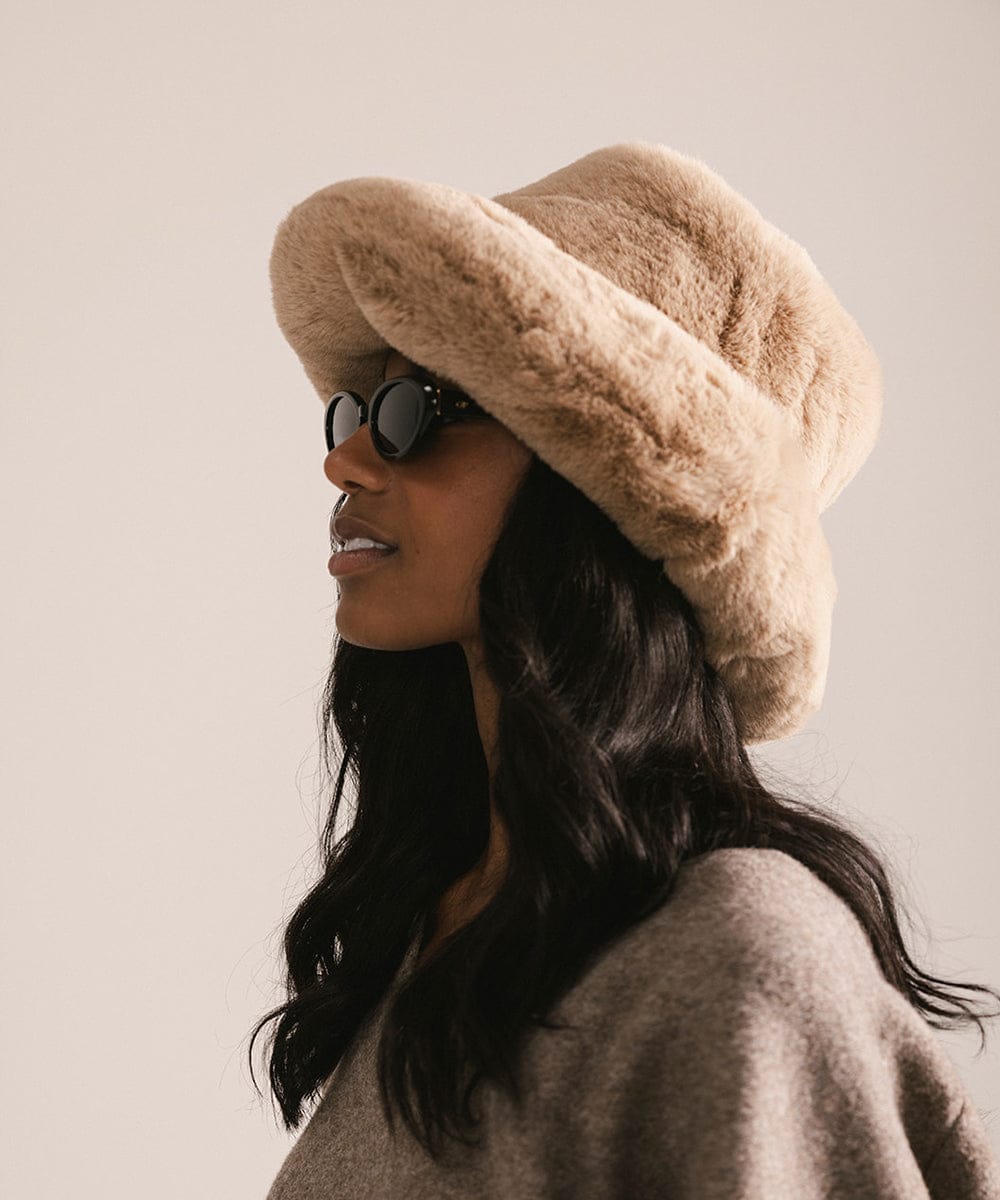 Woman wearing a beige fur hat and sunglasses against a plain background #color_tan