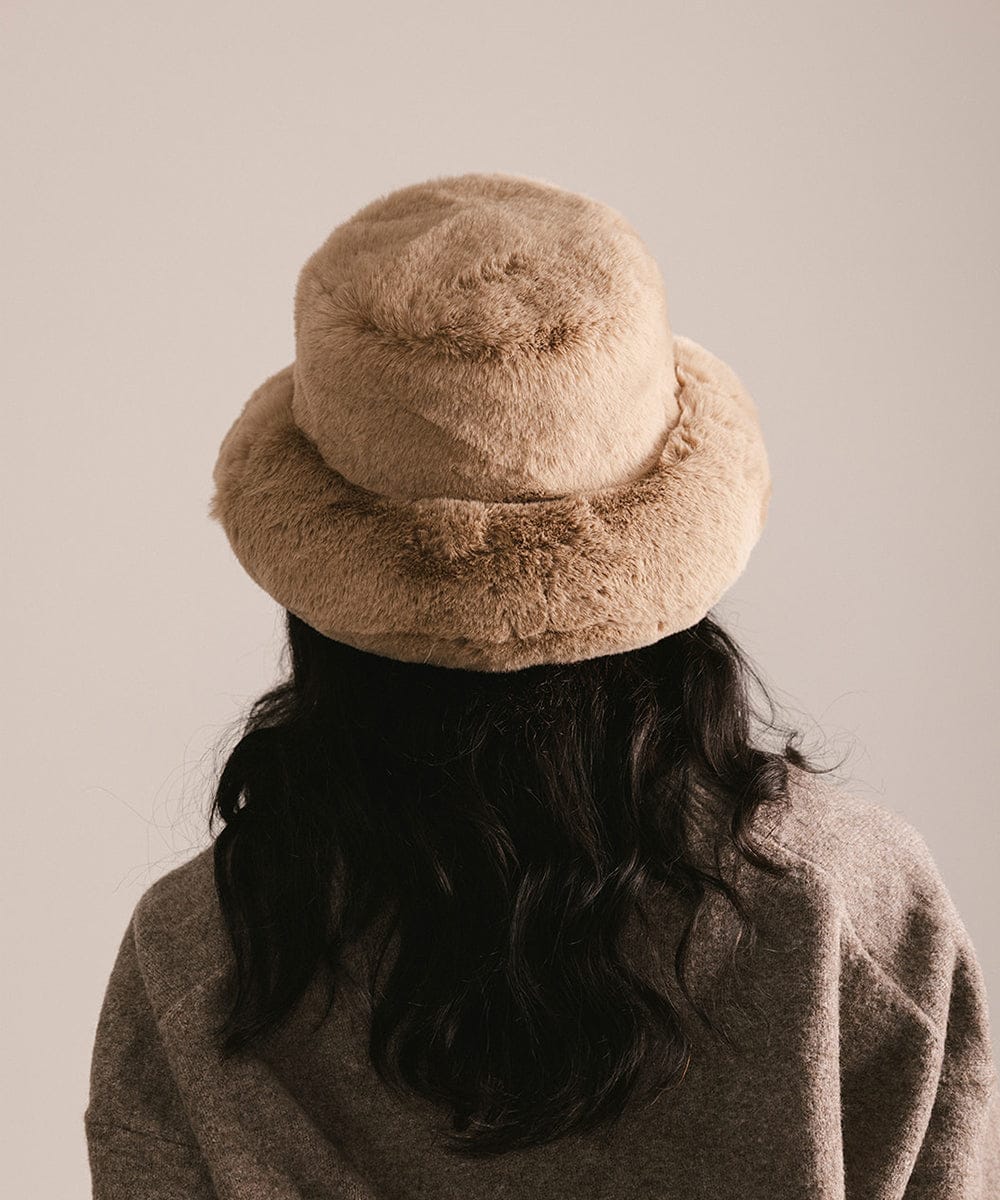 Person wearing a beige bucket hat and coat against a plain background #color_tan