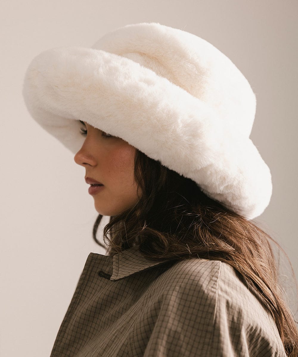 Woman wearing a large white fur hat against a neutral background #color_winter white