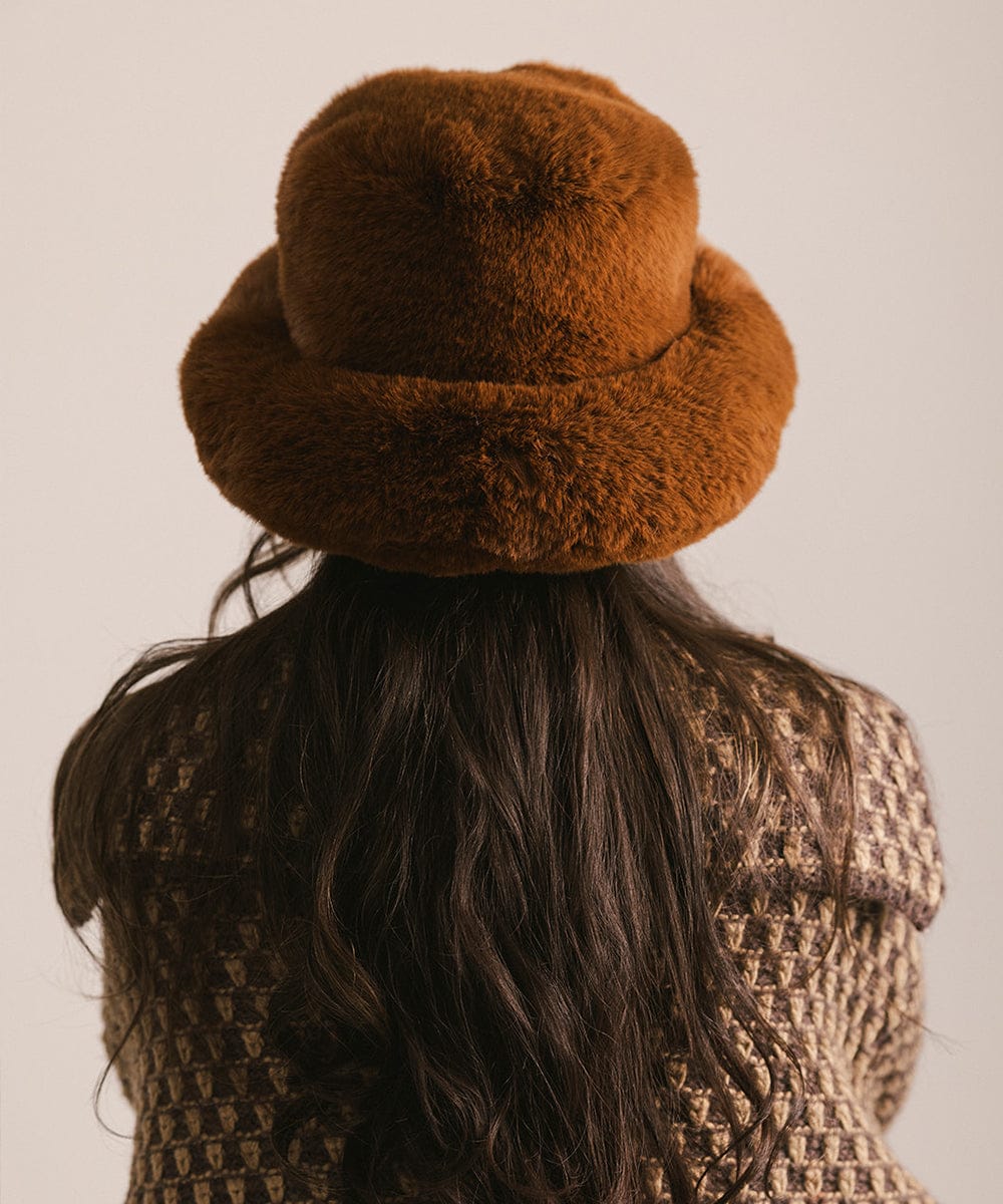 Person wearing a brown fur hat and patterned coat against a neutral background #color_brown