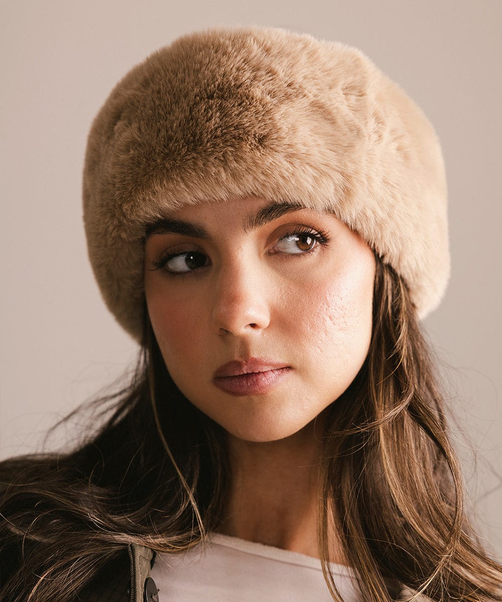 Woman wearing a beige fur hat against a neutral background #color_tan