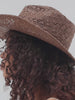 Woman wearing a brown straw hat with a decorative band against a white background #color_chocolate