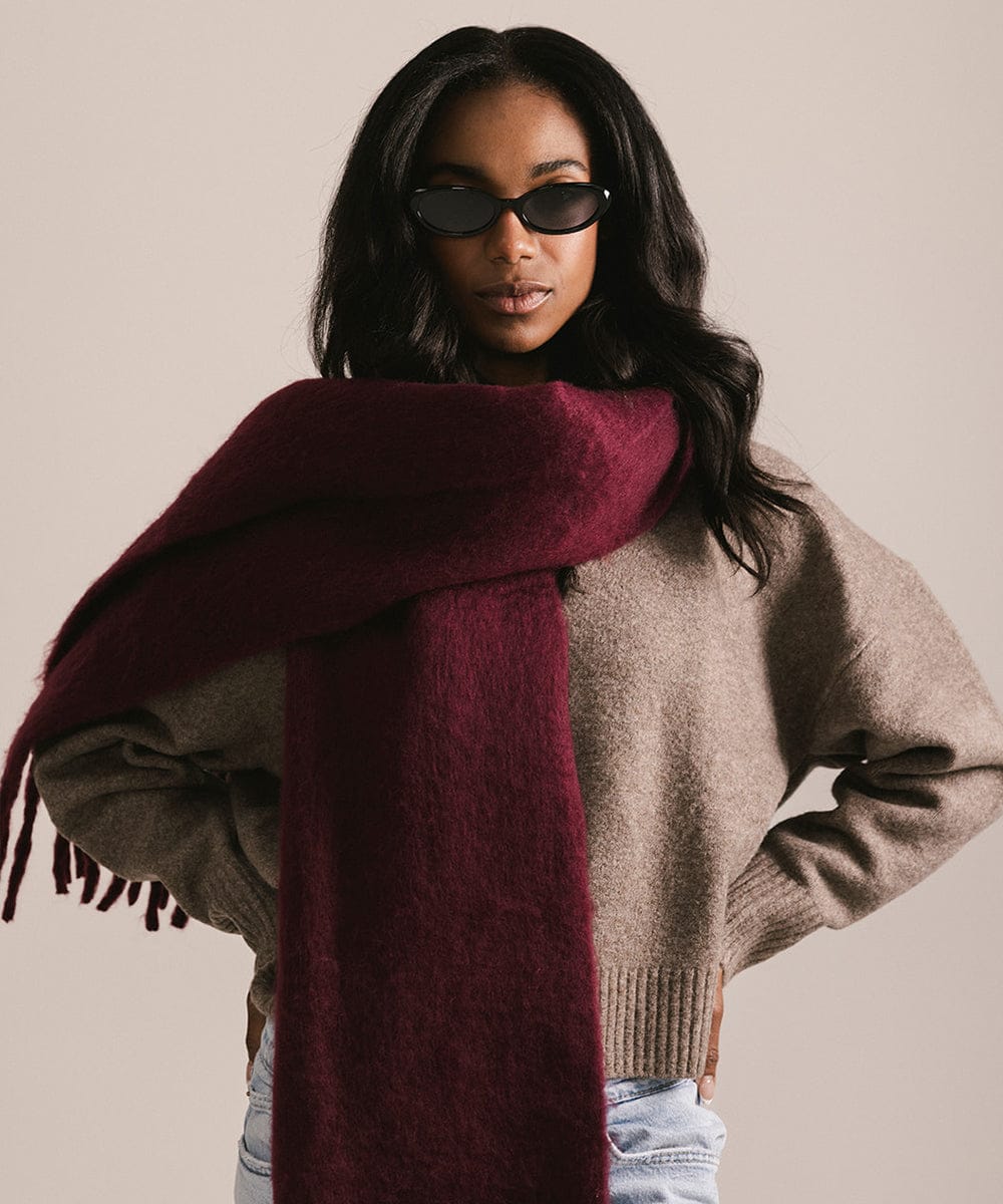 Woman wearing a large burgundy scarf and sunglasses against a neutral background #color_merlot