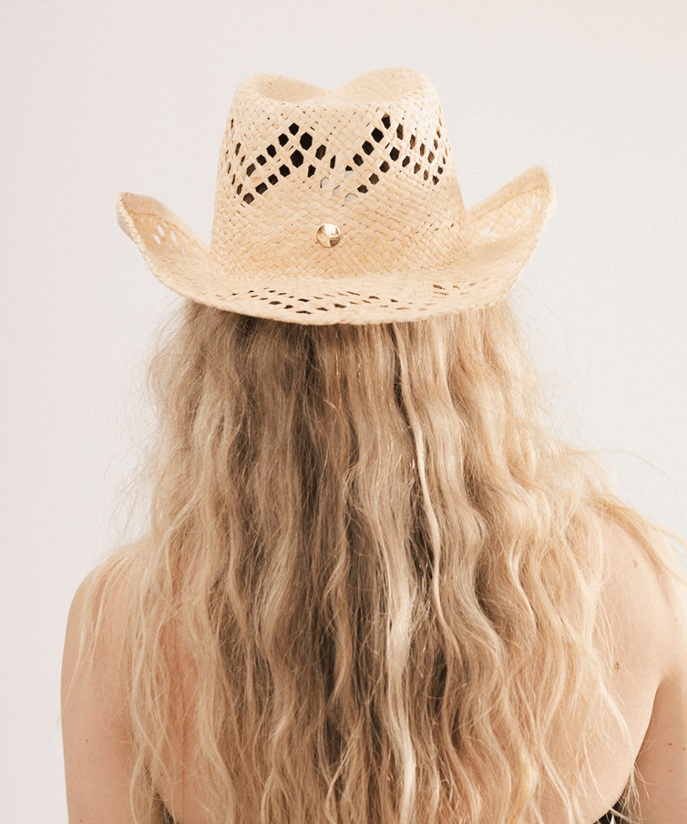 Woman wearing a natural colored straw cowboy hat and dark clothing against a plain background #color_natural