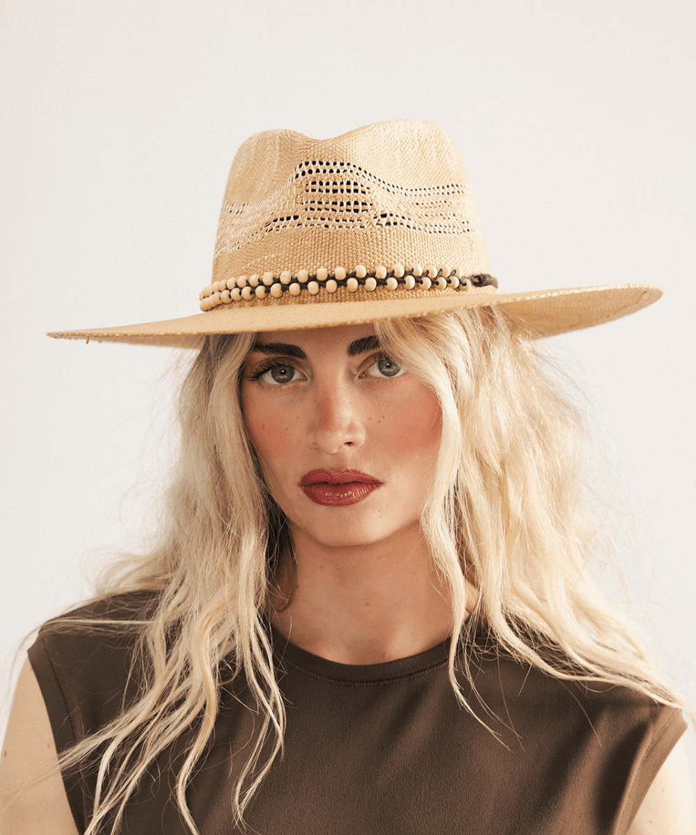 Woman wearing a washed tan straw fedora hat and dark clothing against a plain background #color_washed tan