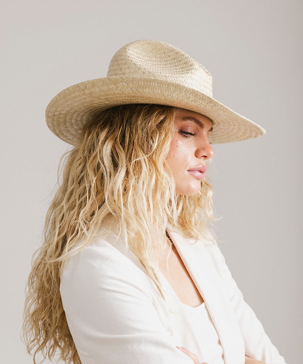 Woman wearing a natural colored straw cowboy hat and a white coat, posing sideways against a plain background  #color_natural