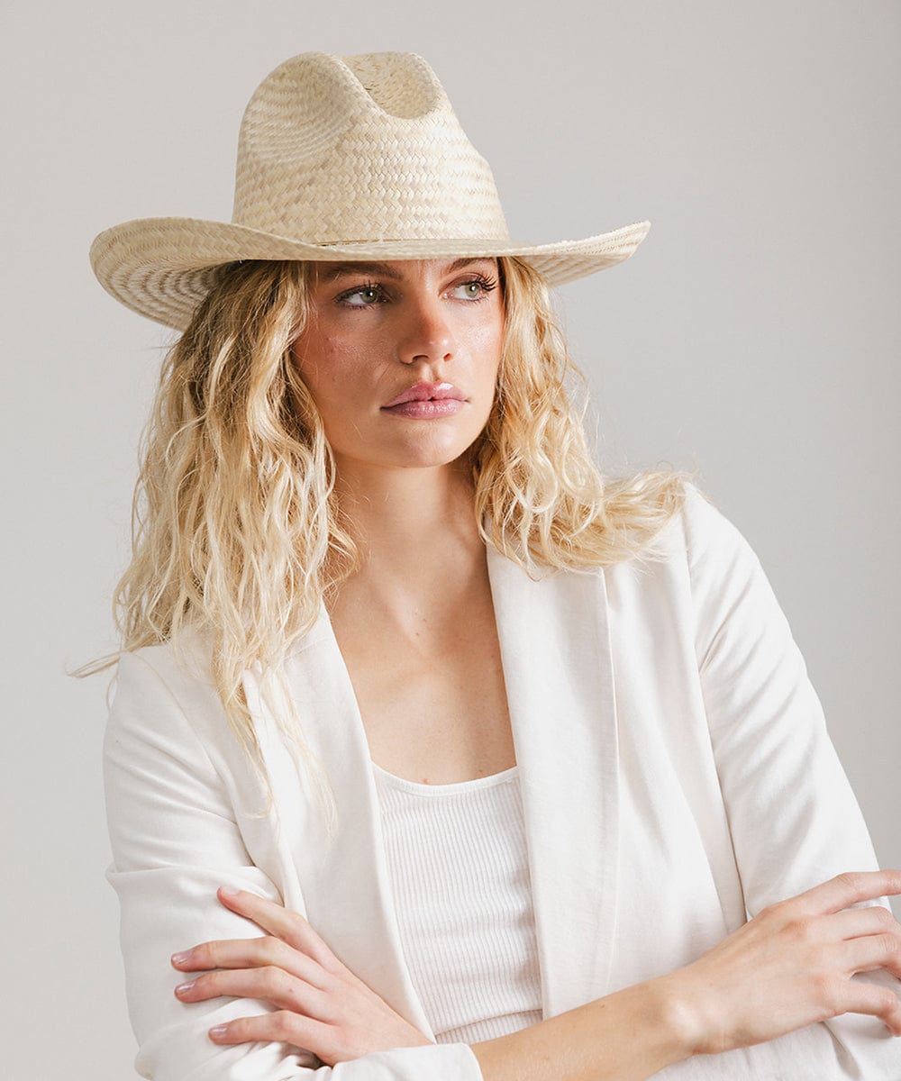 Woman wearing a natural colored straw cowboy hat and a white coat against a plain background  #color_natural