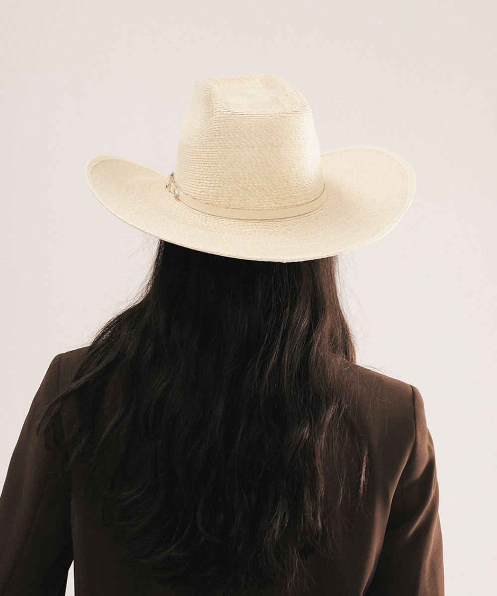 Woman wearing a natural colored straw cowgirl hat and brown blazer on a light background #color_natural