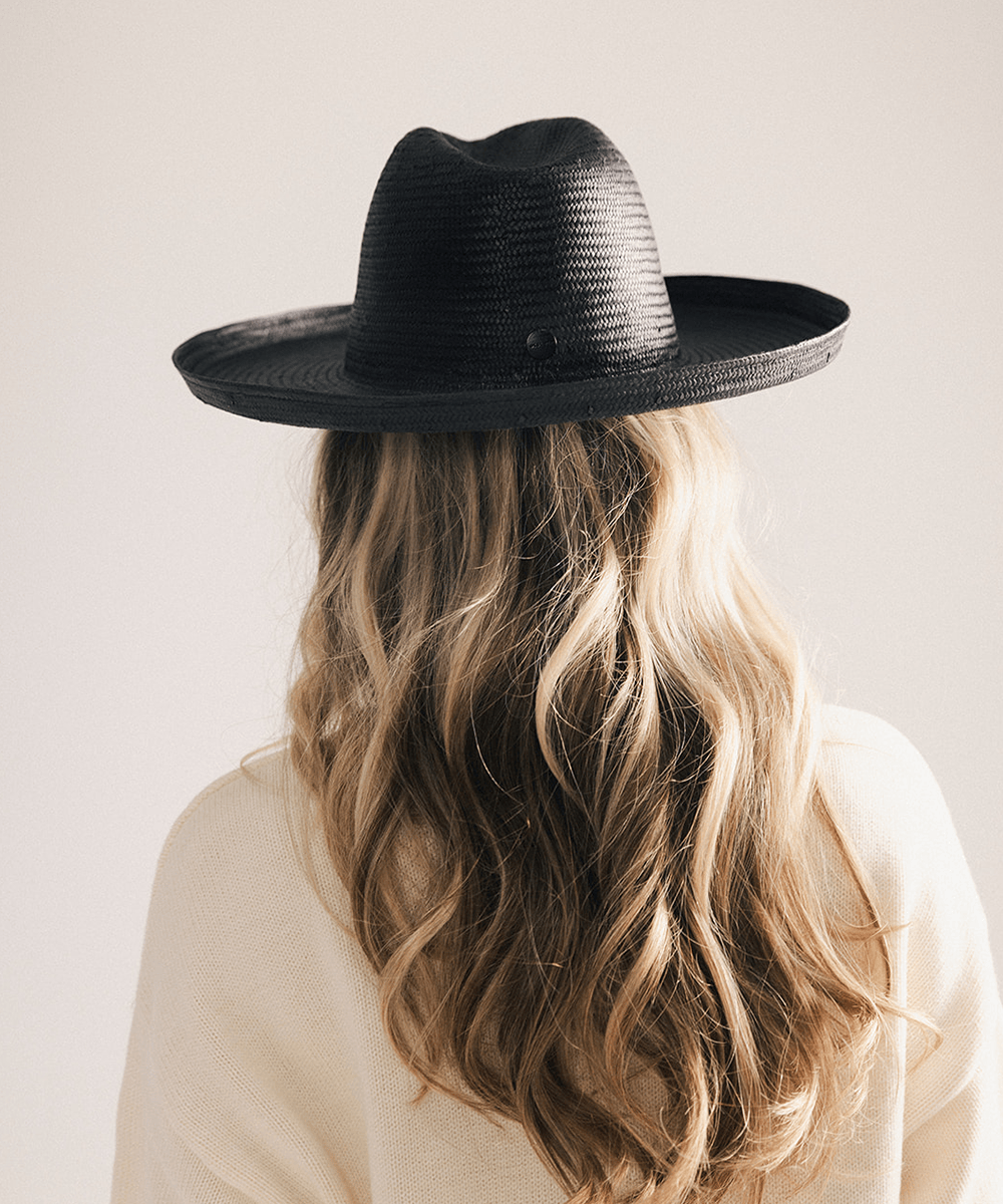 Woman wearing a black pencil brim fedora hat made of paper straw, displayed against a white background. #color_black