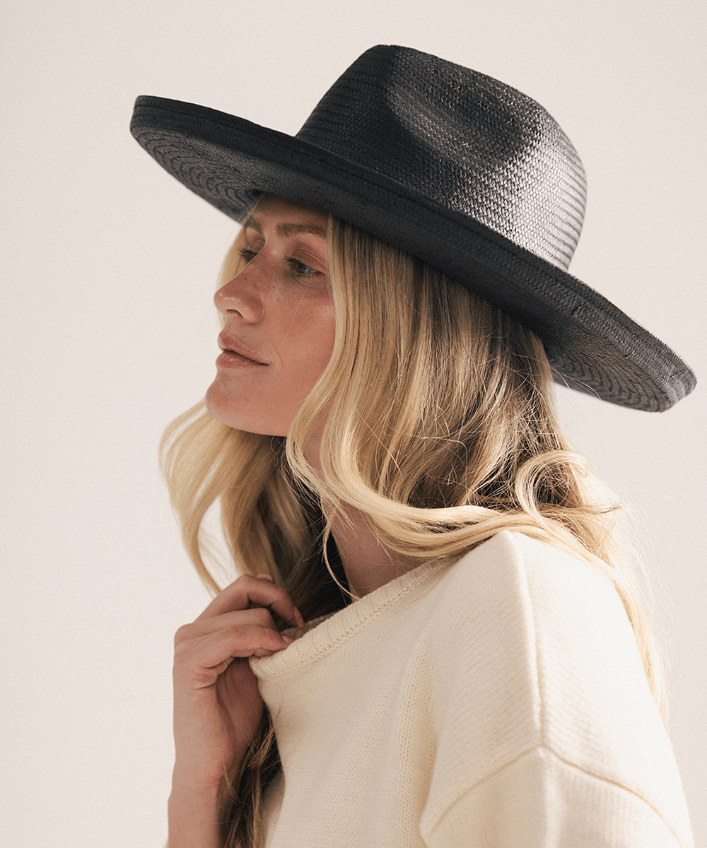 Woman wearing a black pencil brim fedora hat made of paper straw, displayed against a white background. #color_black