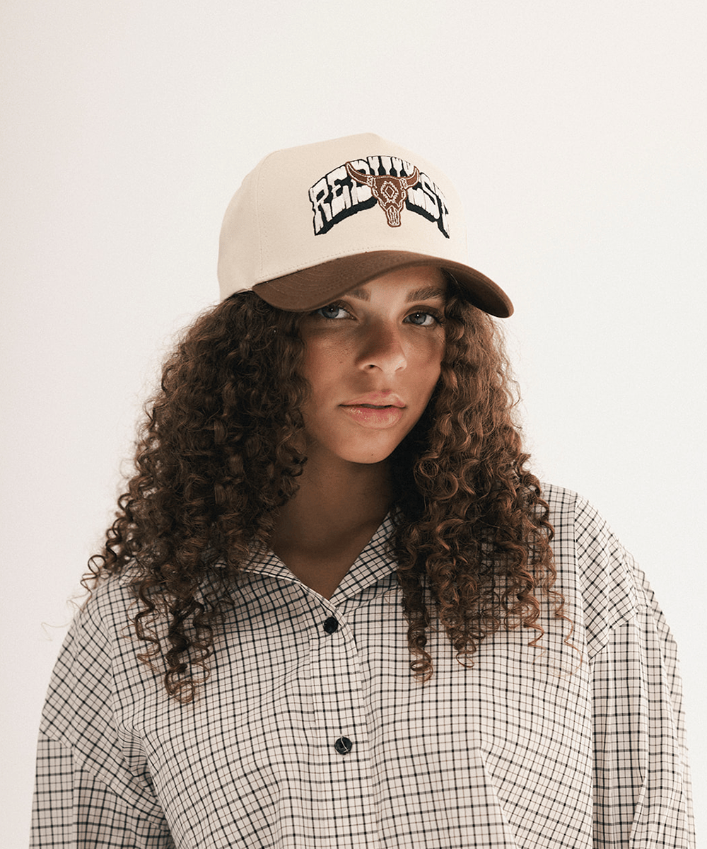 Woman wearing a beige and brown cap with bull logo on a white background #color_cream - brown