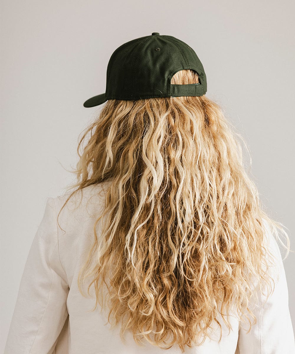 Woman with long hair wearing a dark green cap and a white coat against a plain background  #color_dark green