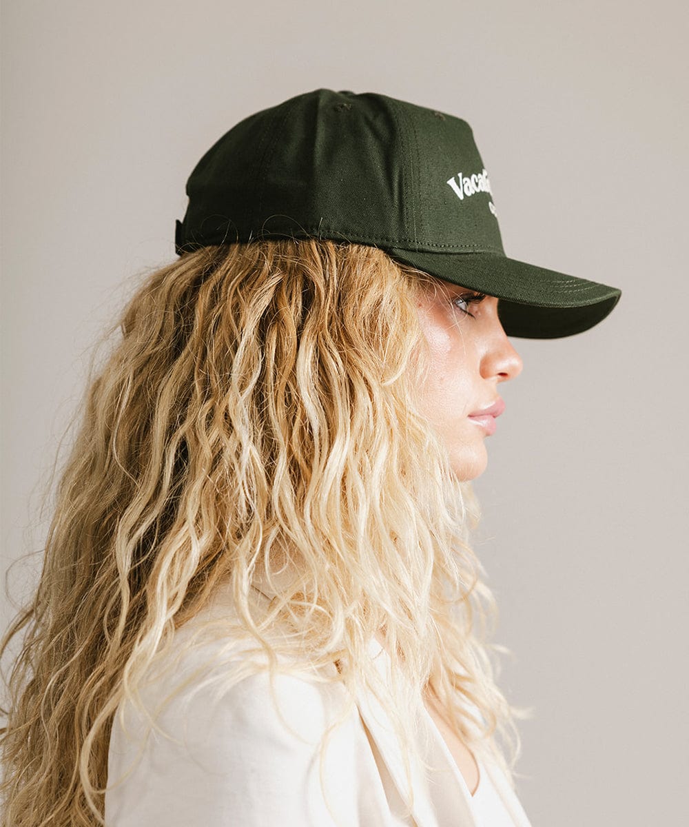 Woman wearing a dark green cap and a white coat, facing sideways  against a plain background  #color_dark green