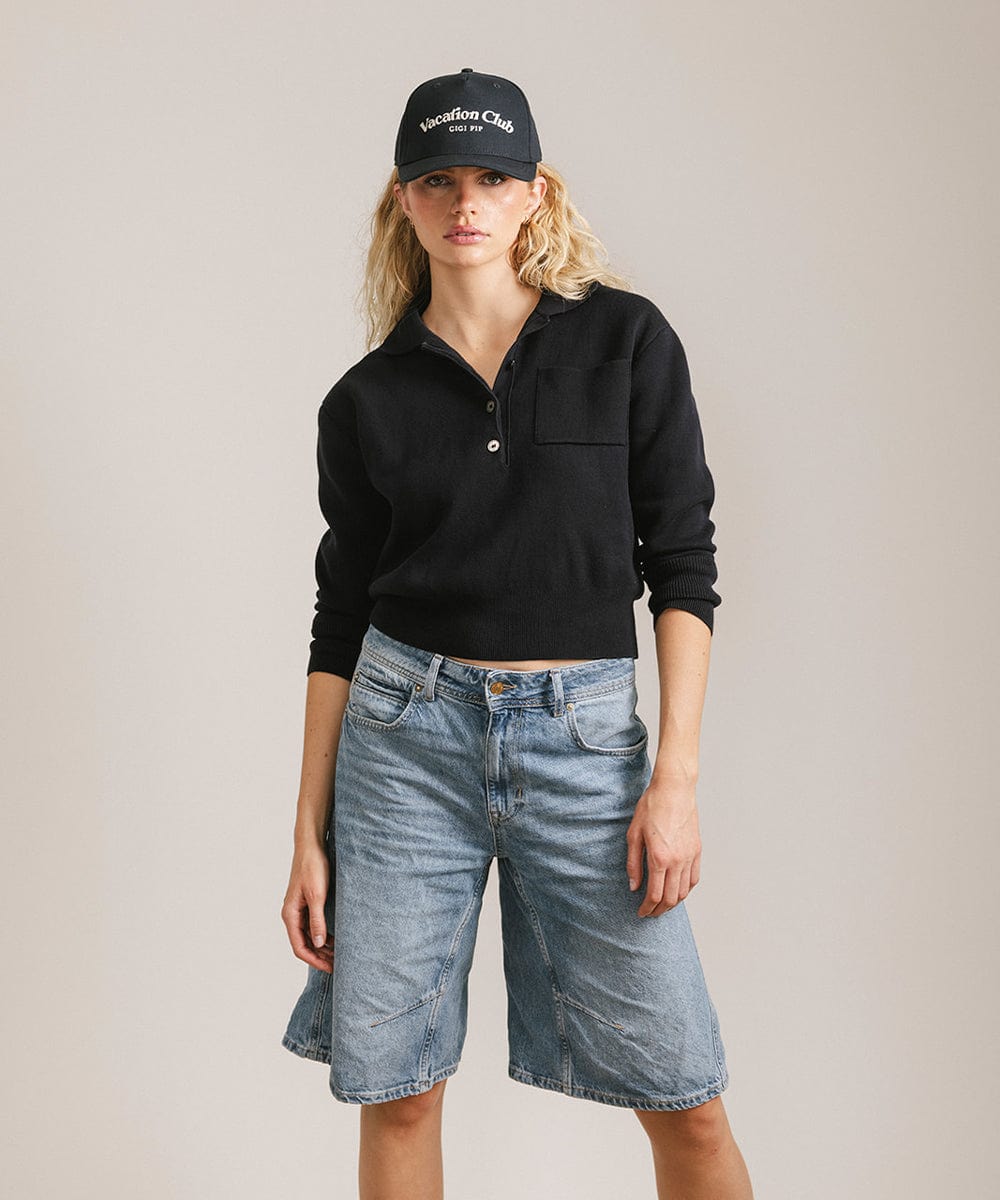 Woman wearing a navy cap with 'Vacation Club' text, a black shirt and denim shorts against a plain background  #color_navy