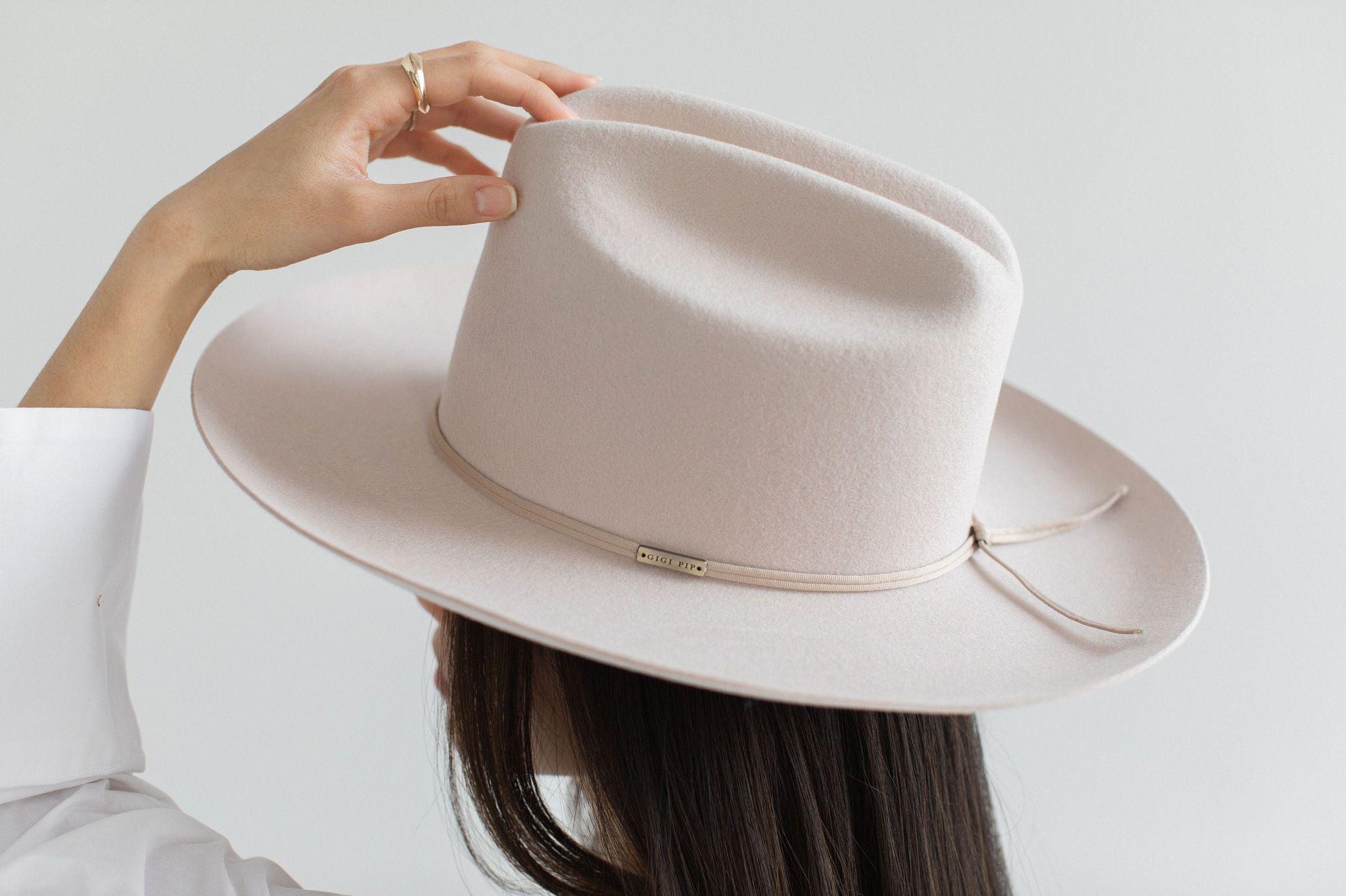 Close up image of a woman wearing a ivory colored cowboy hat with a hat band facing behind against a plain background #color_ivory