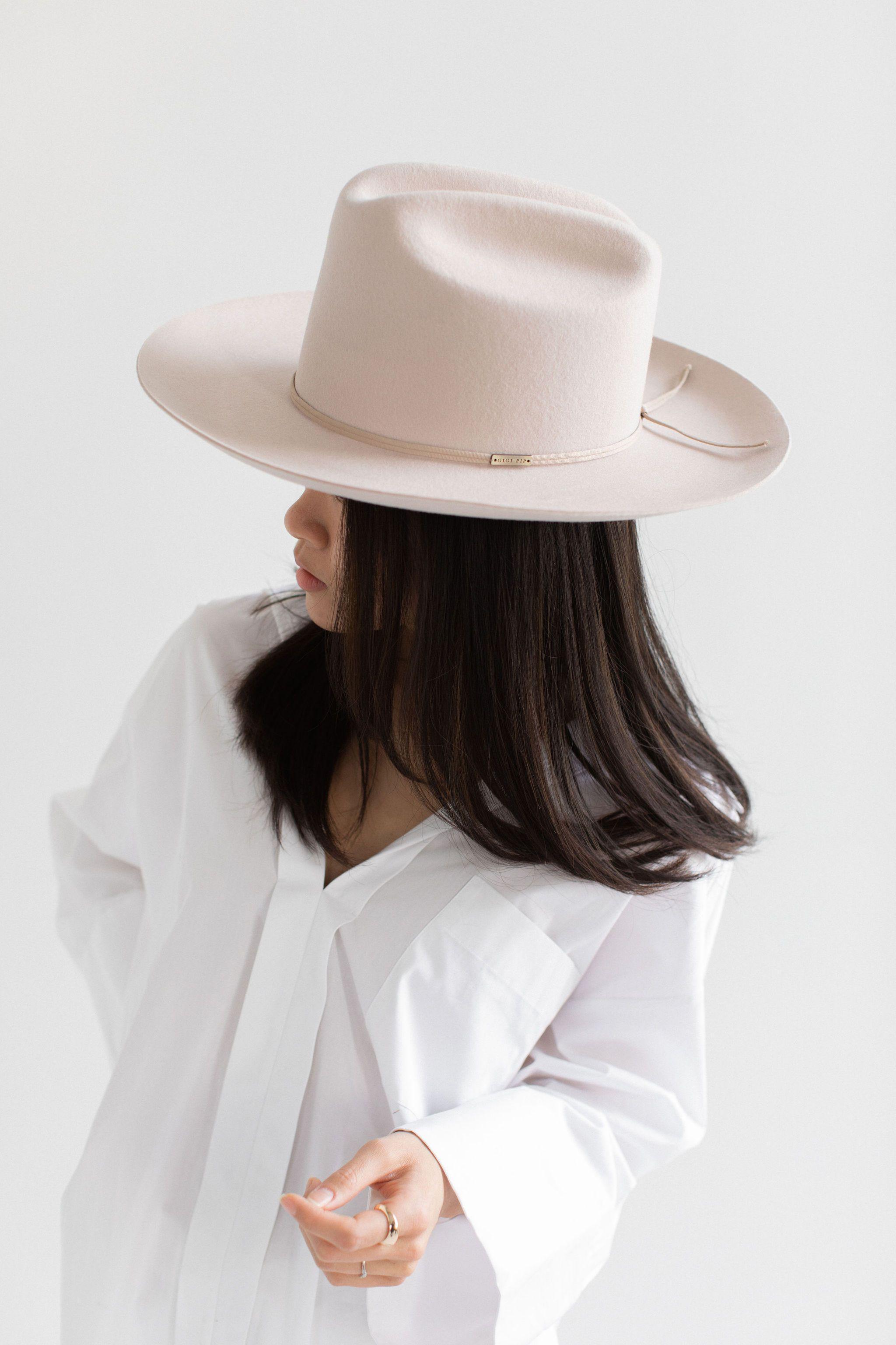 Woman wearing a ivory colored cowboy hat with a hat band and a white shirt, looking sideways against a plain background #color_ivory