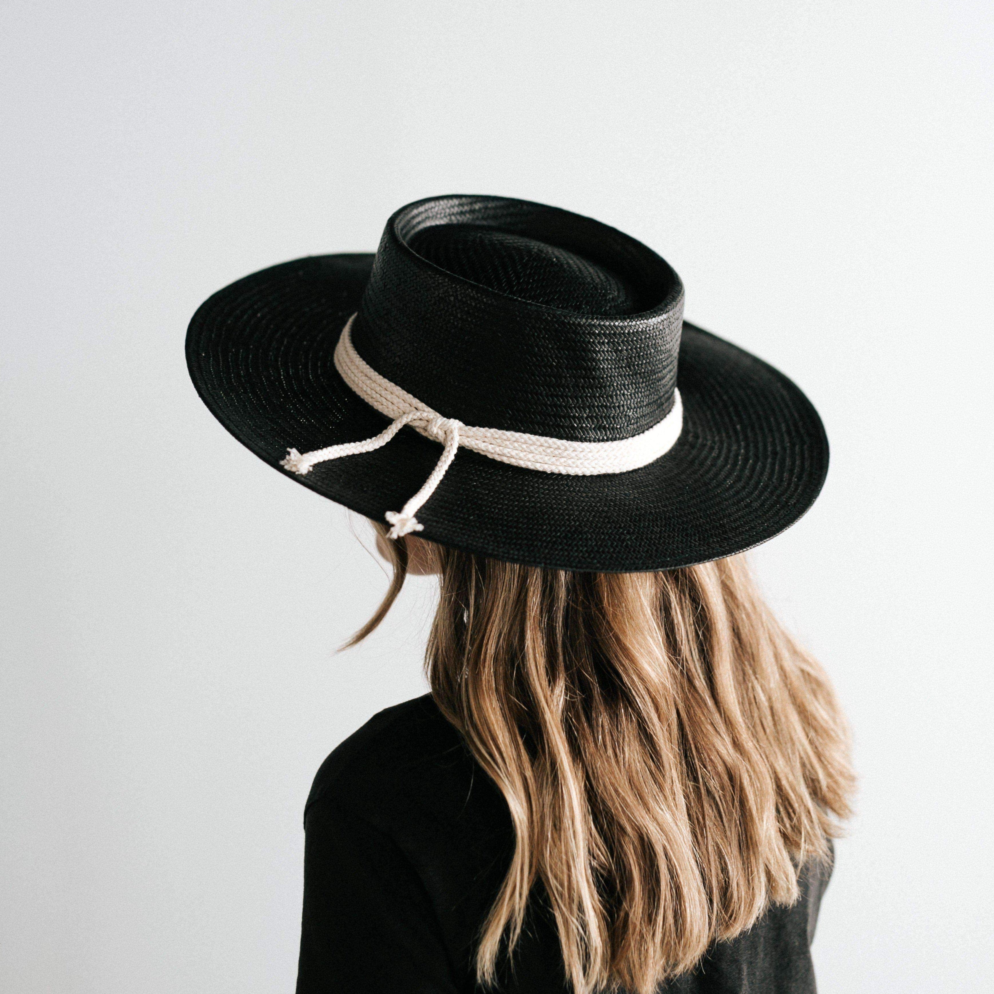 Woman wearing a black straw hat with a hat band and a black t-shirt, posing sideways against a plain background #color_black