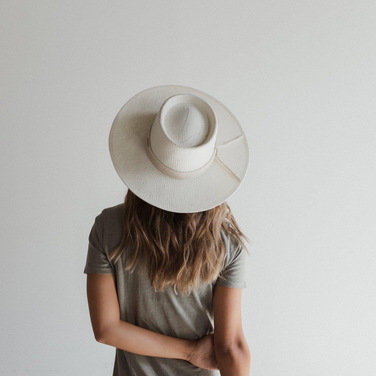 Woman wearing an ivory colored straw hat with a hat band and a grey t-shirt, facing behind against a plain background #color_ivory