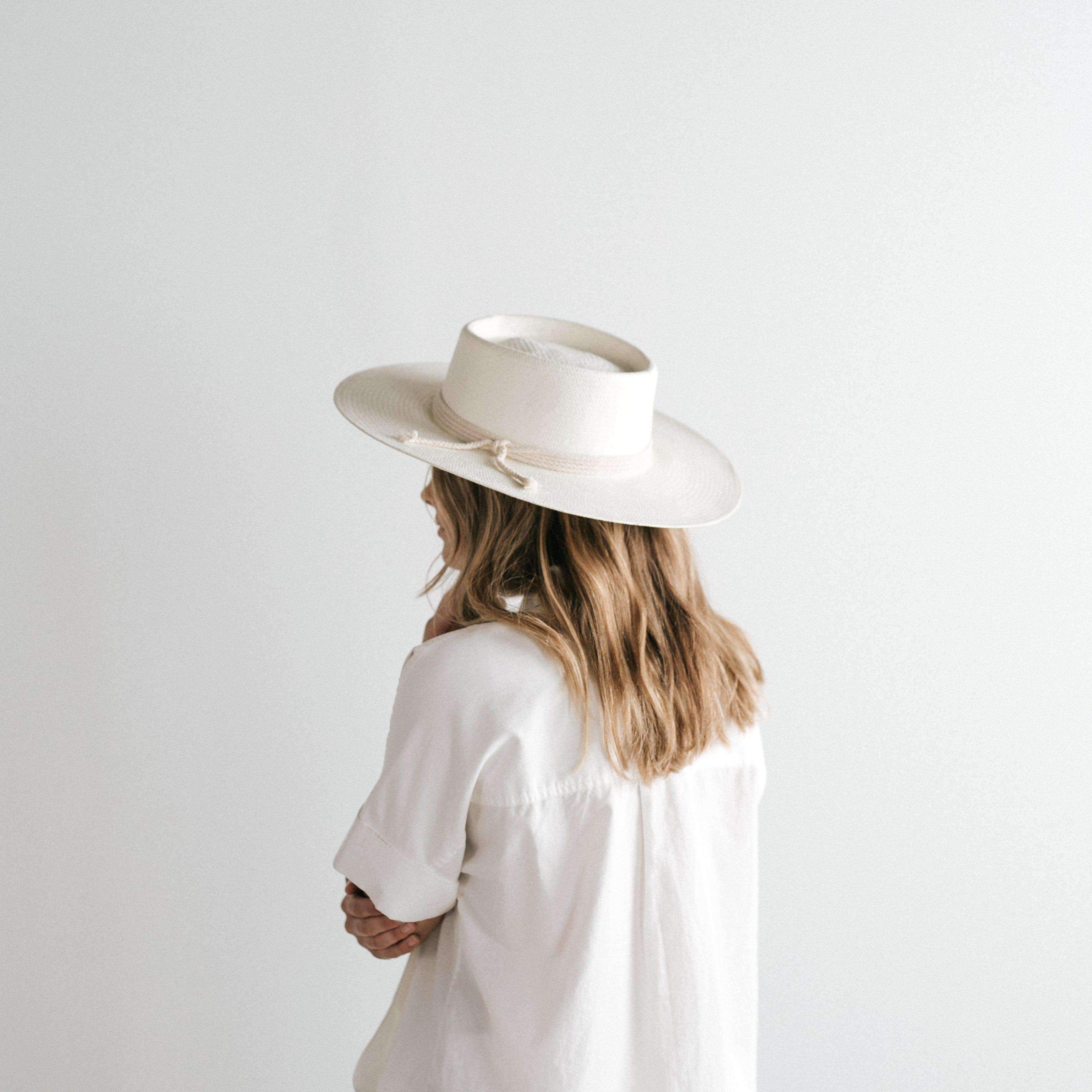 Woman wearing an ivory colored straw hat with a hat band and a white t-shirt, facing sideways against a plain background #color_ivory