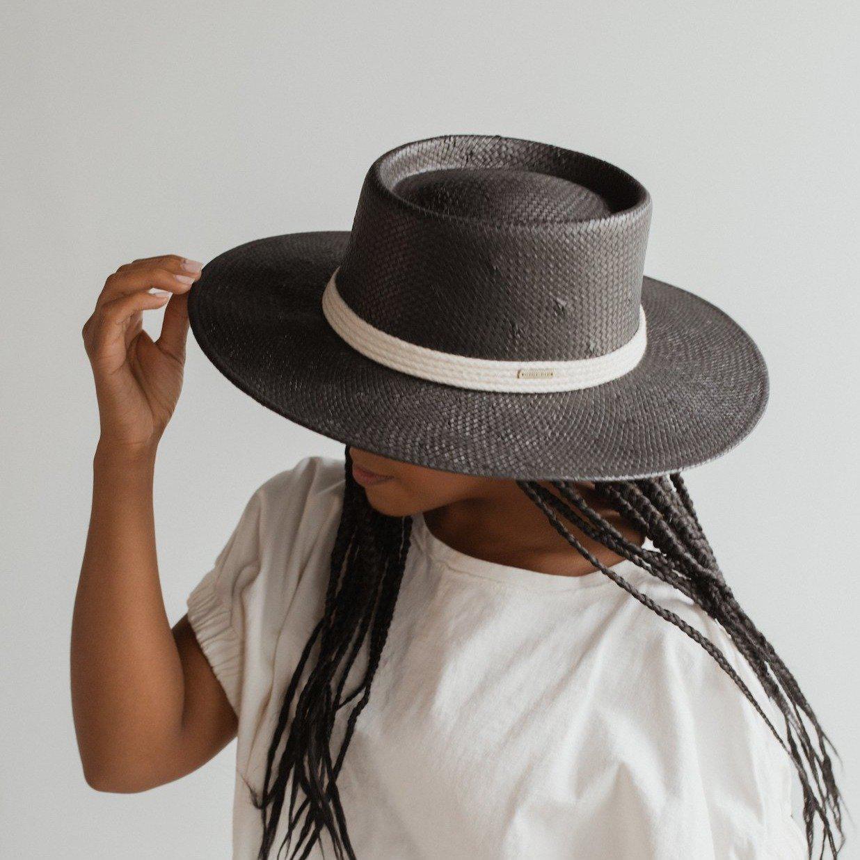 Woman wearing a black straw hat with a hat band and a white t-shirt, posing sideways against a plain background #color_black
