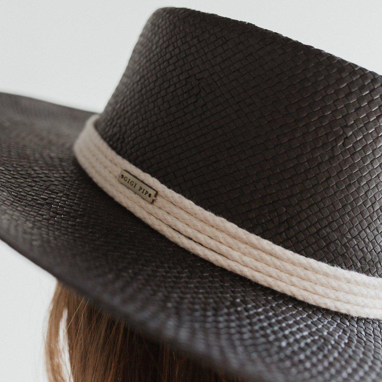 Close up image of a black straw hat with a hat band with the brand logo against a plain background #color_black