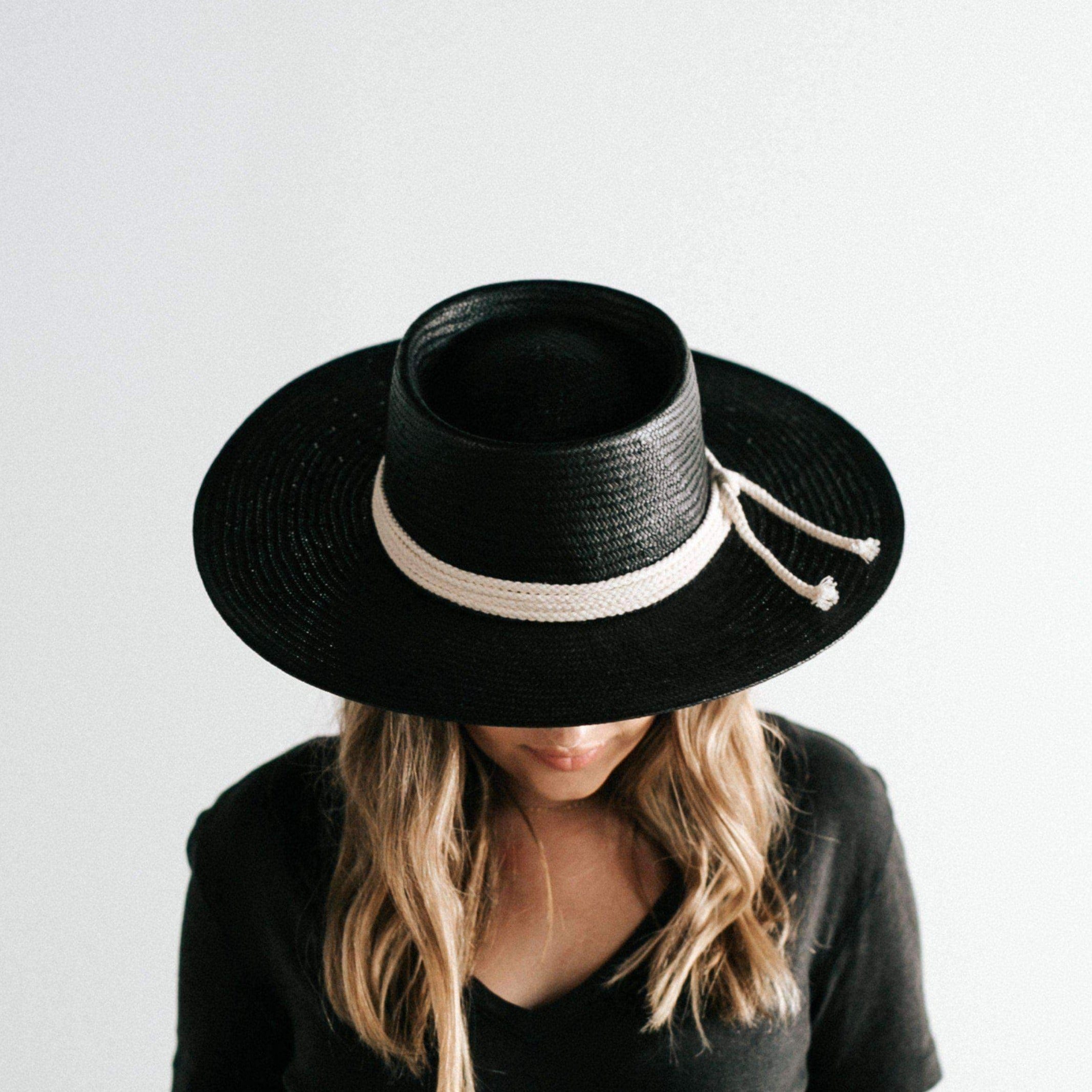 Woman wearing a black straw hat with a hat band and a black t-shirt against a plain background #color_black