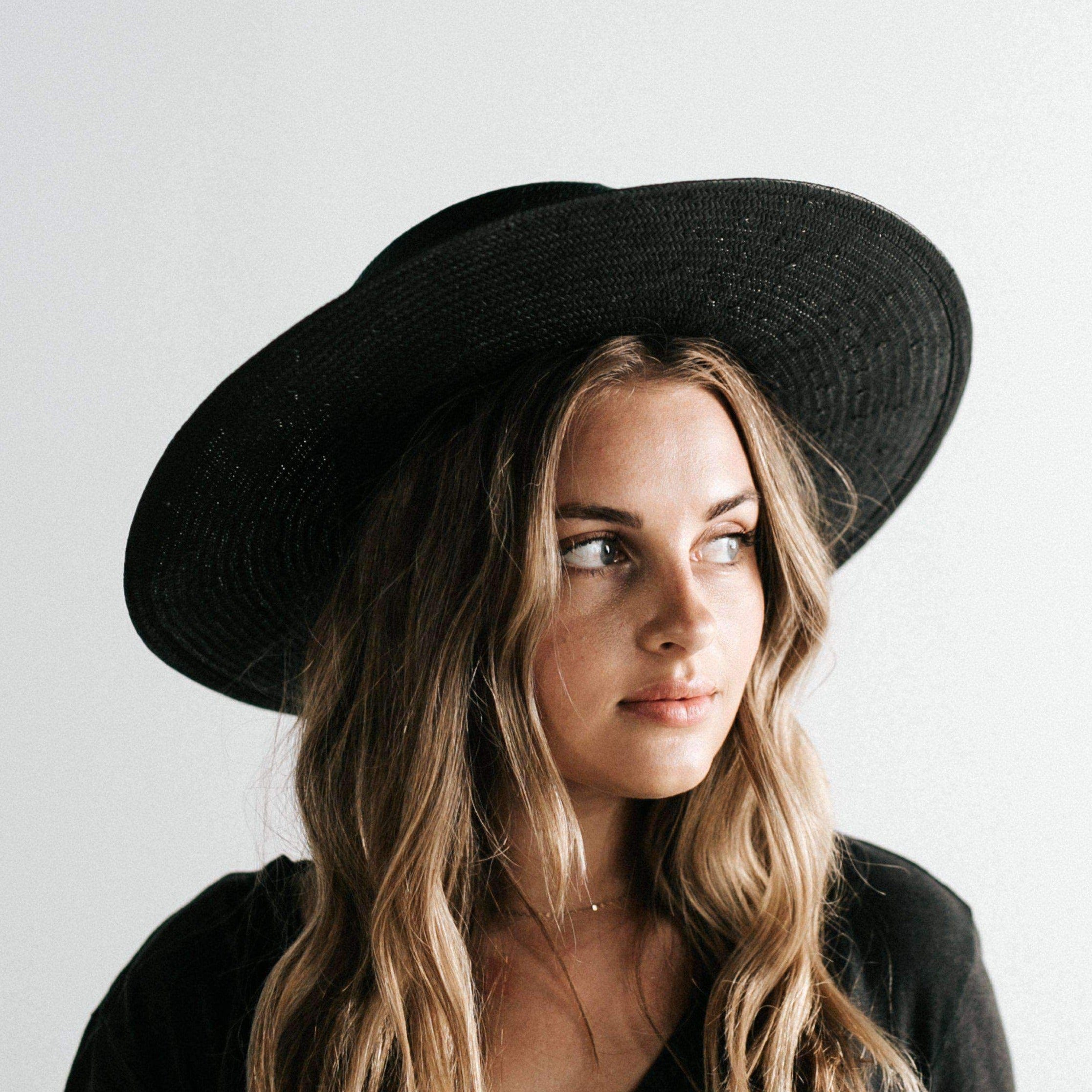 Woman wearing a black straw hat with a hat band and a black t-shirt, looking sideways against a plain background #color_black