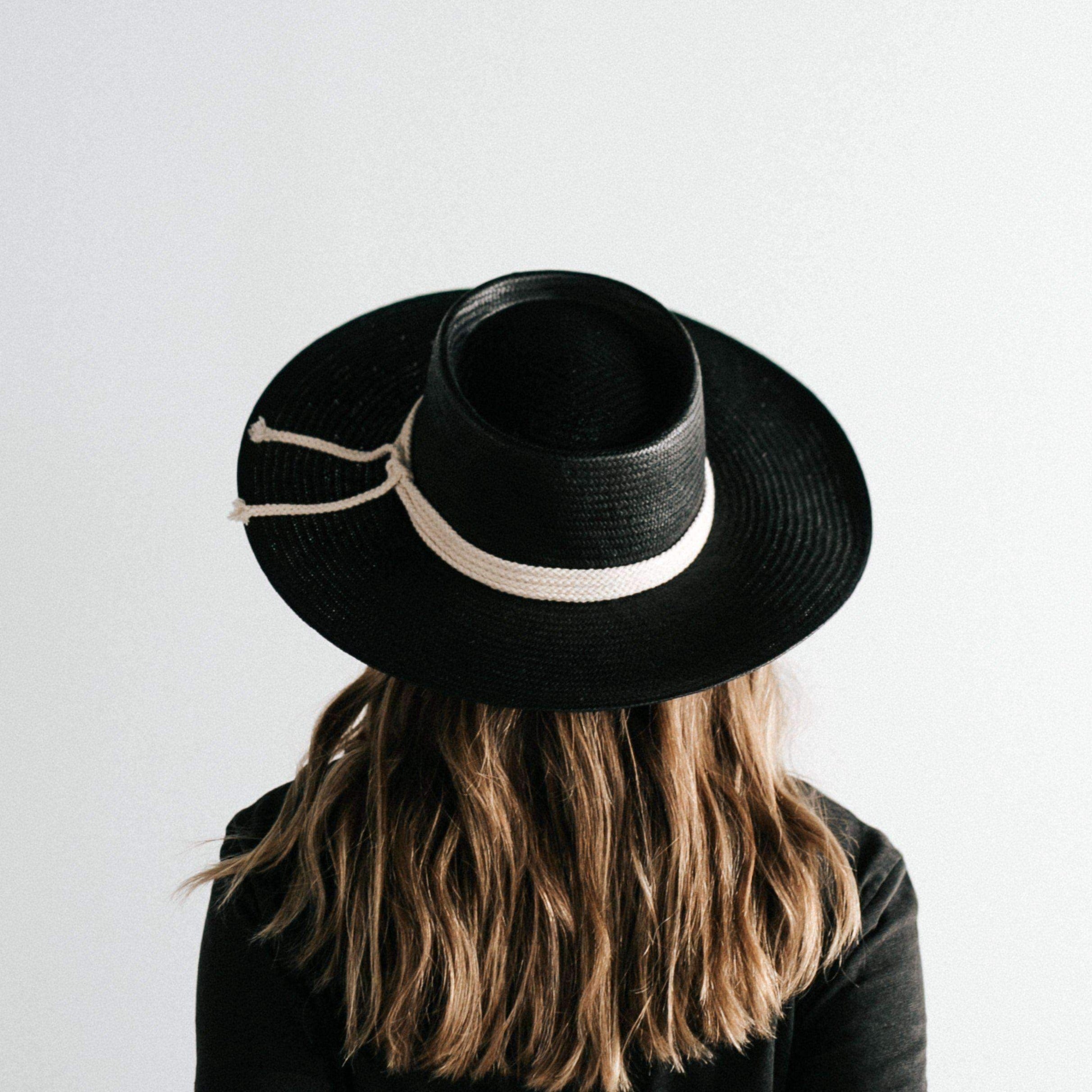 Woman wearing a black straw hat with a hat band and a black t-shirt, facing behind against a plain background #color_black