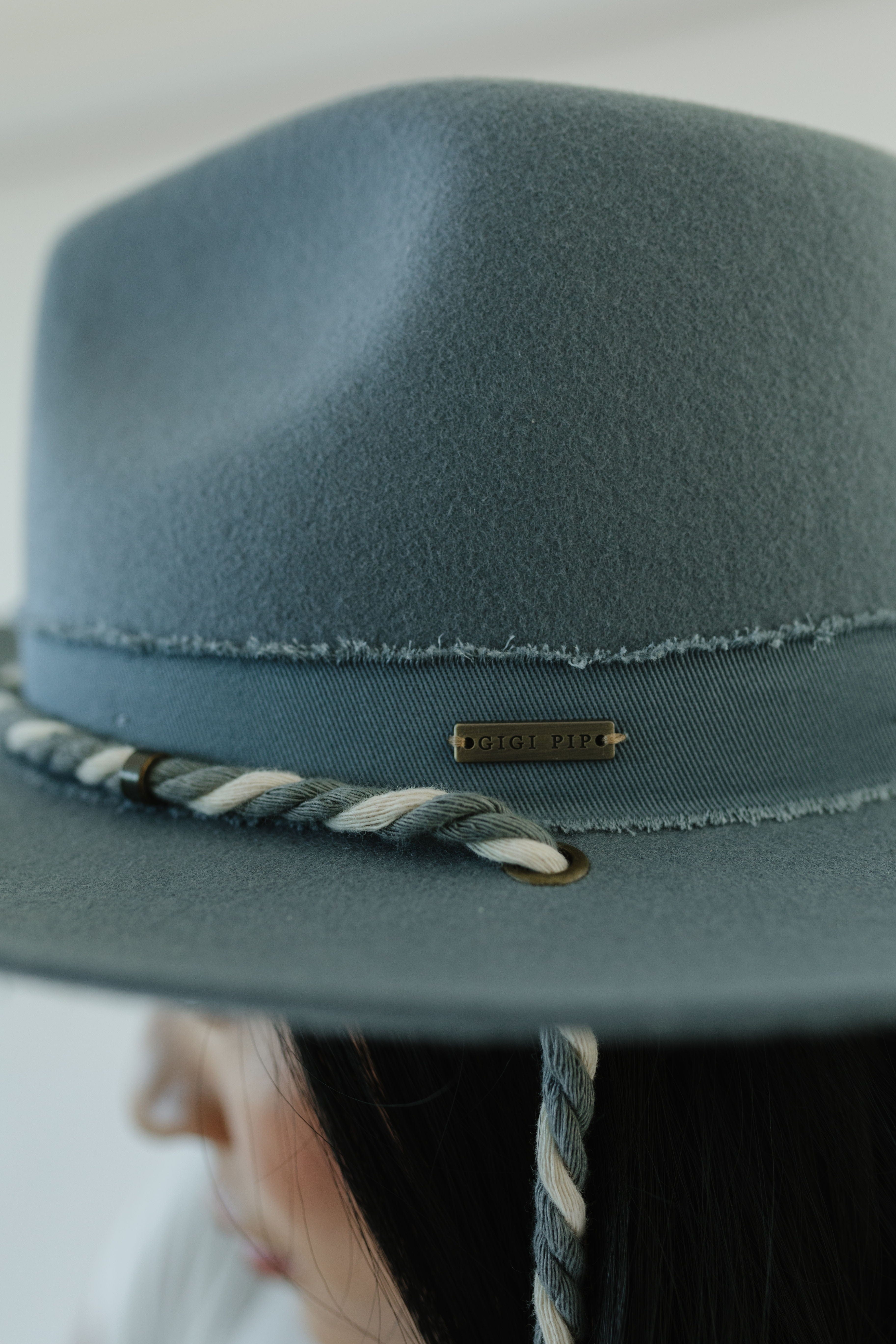 Close up image of someone wearing a denim colored wide brim hat with a  braided chin strap against a plain background  #color_denim