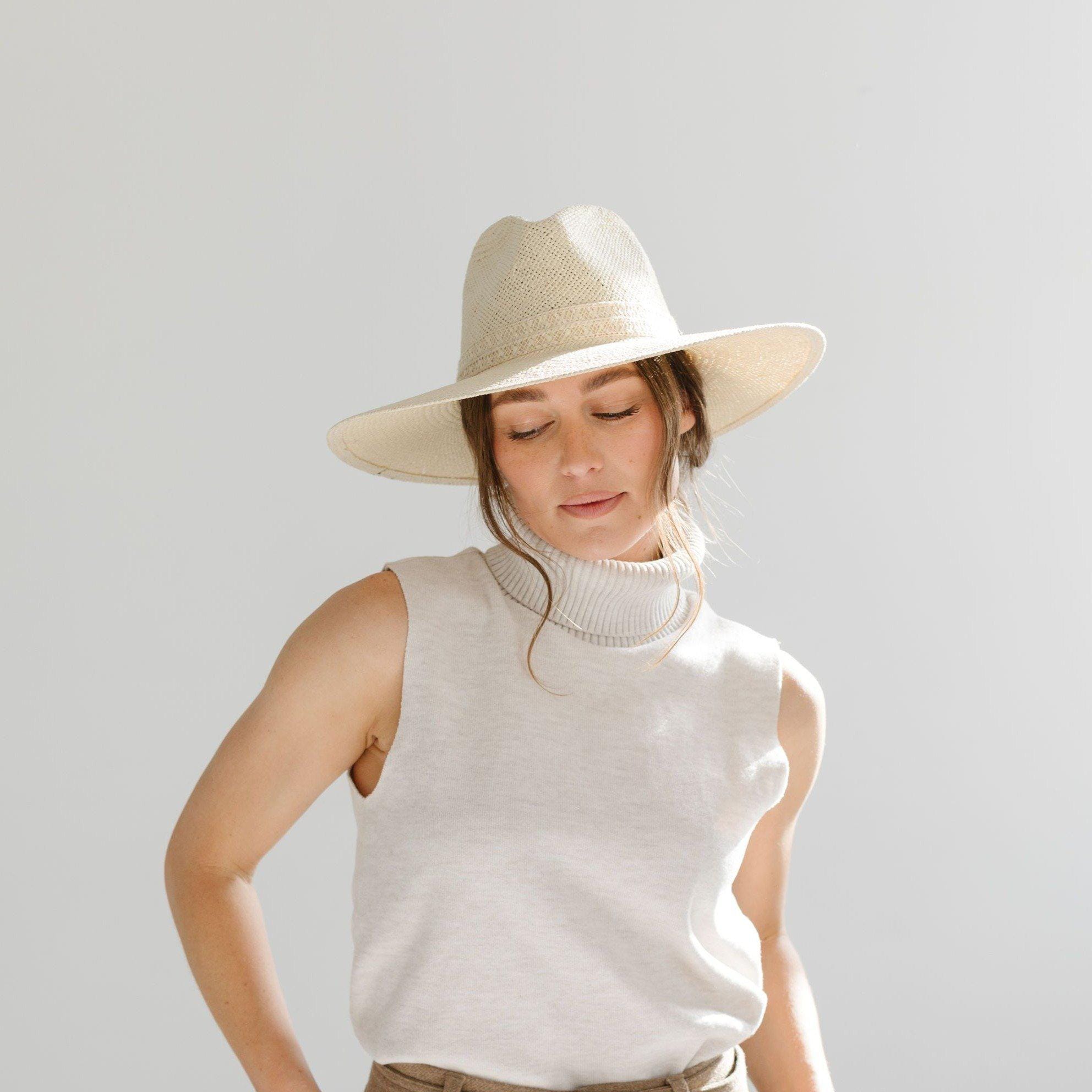 Woman wearing a cream straw hat and a white sleeveless top against a plain background #color_cream