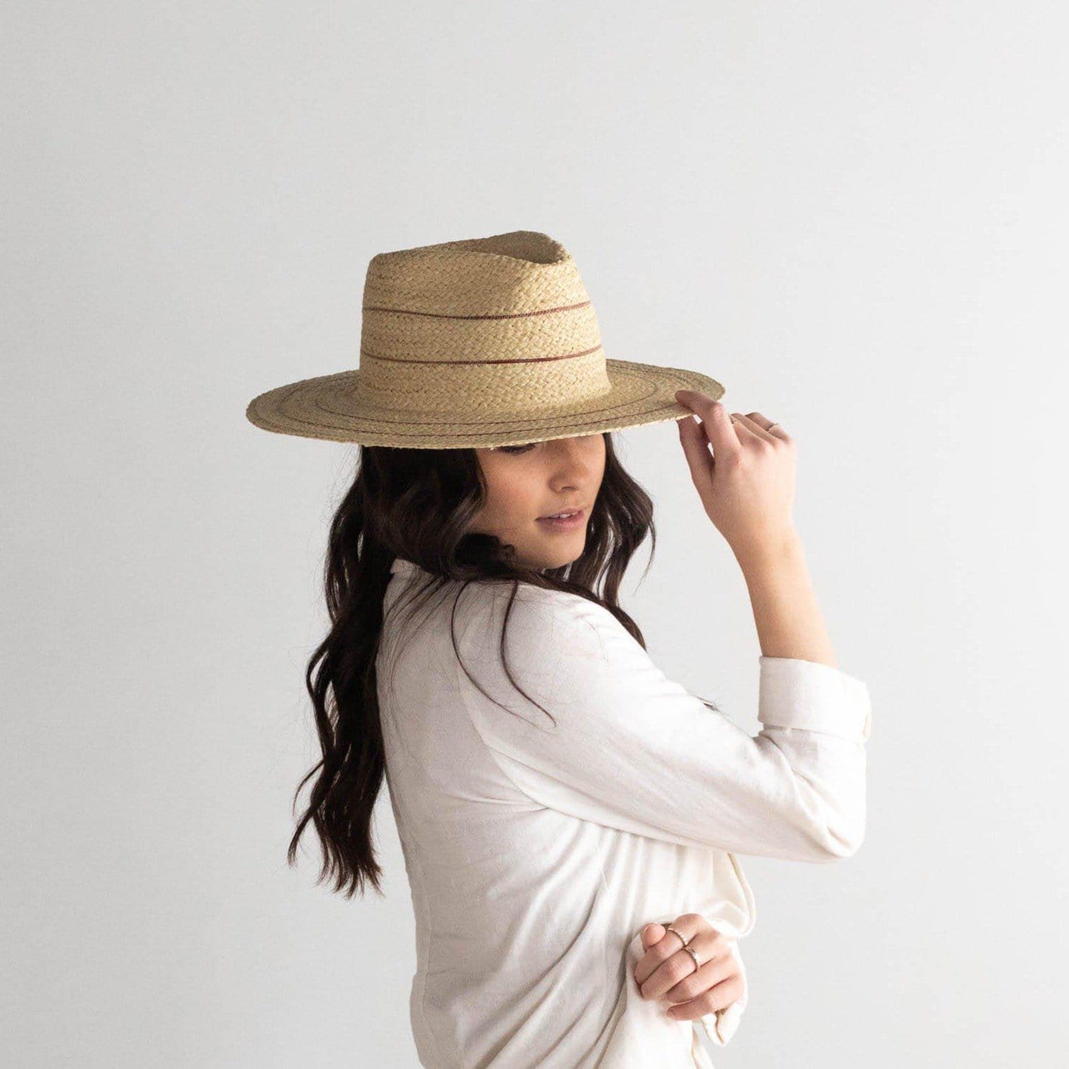 Woman wearing a natural colored straw fedora hat with stripes and a  cream jacket, posing against a plain background #color_natural with stripes