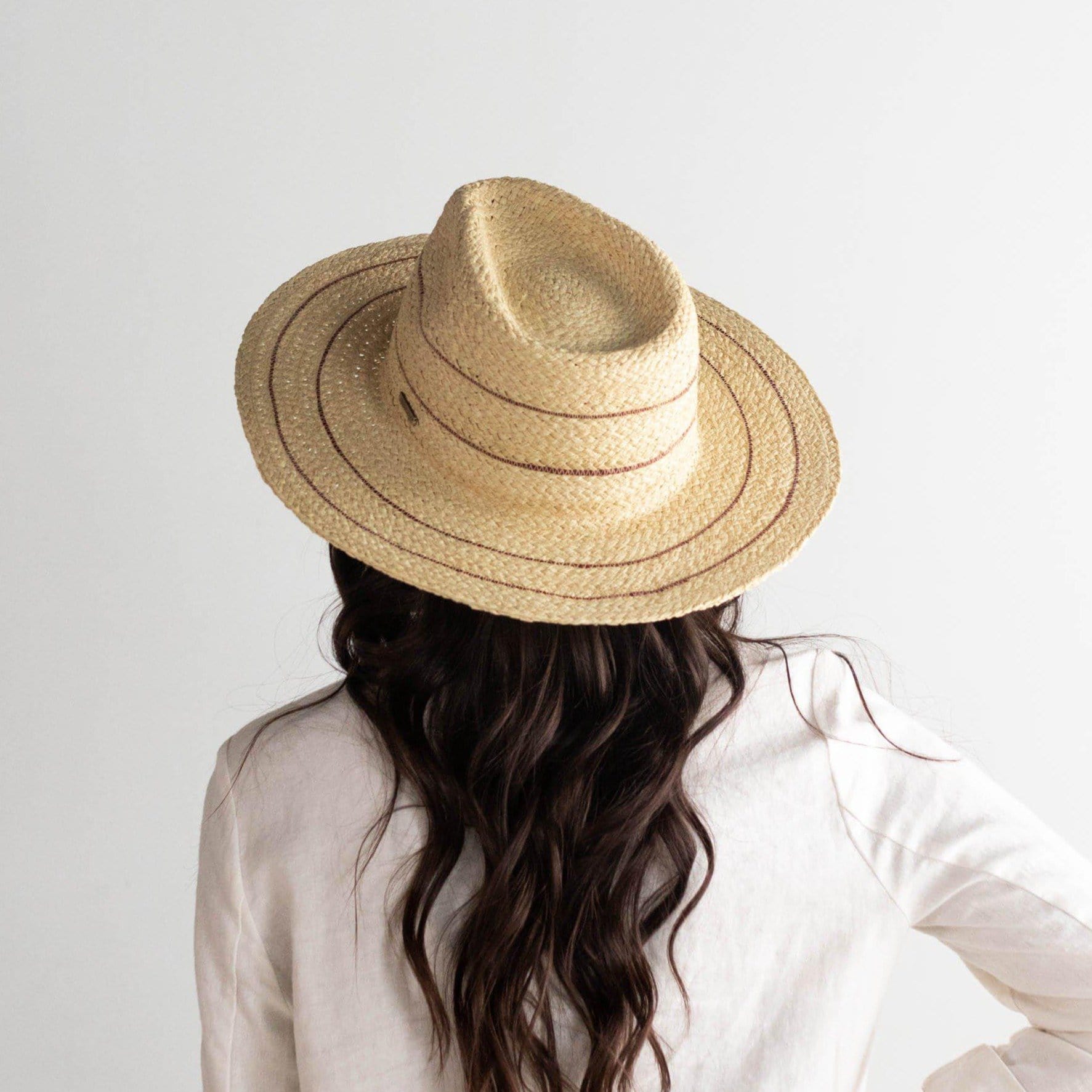 Woman wearing a natural colored straw fedora hat with stripes and a  cream jacket, facing behind against a plain background #color_natural with stripes