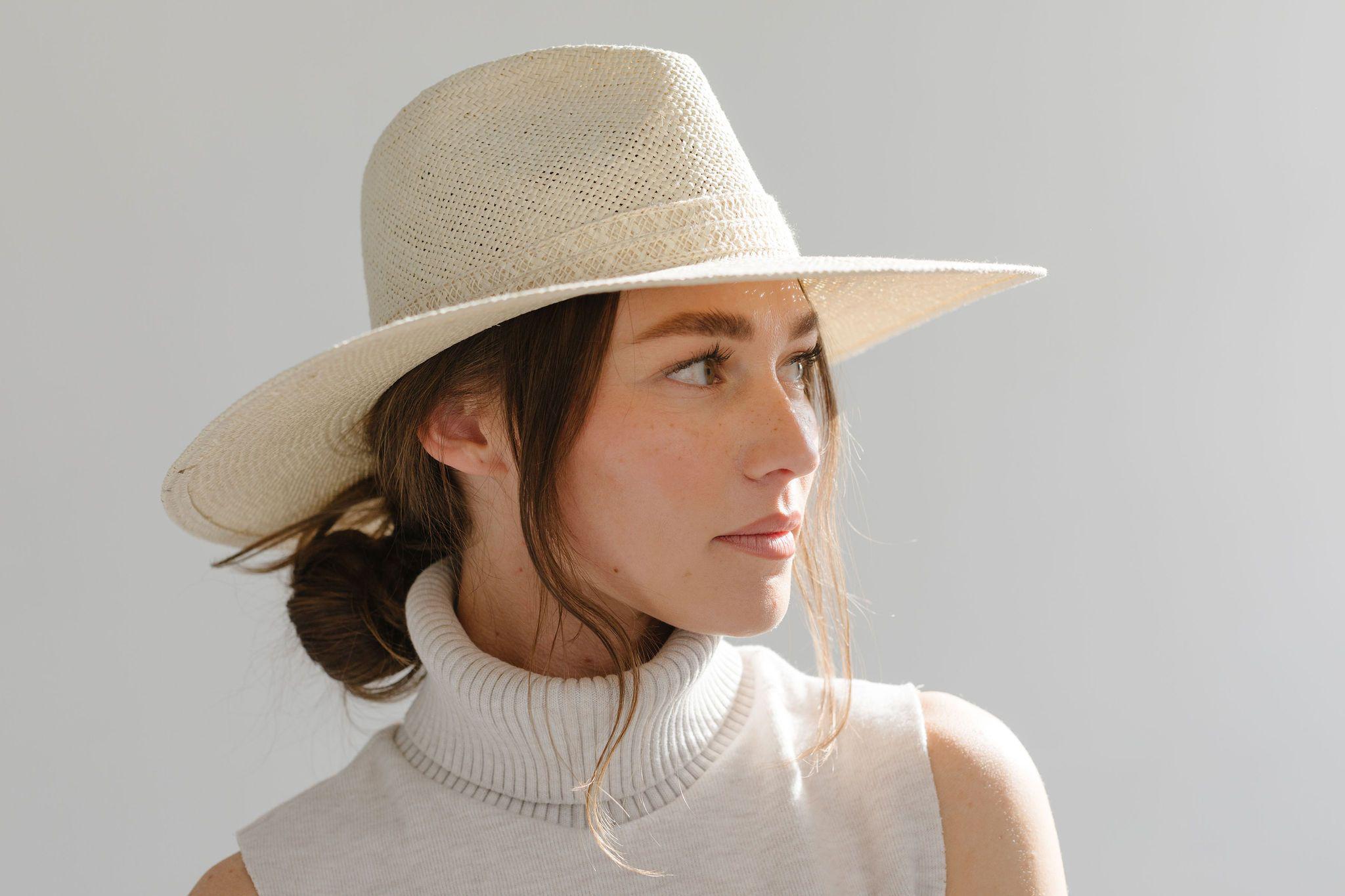 Woman wearing a cream straw hat and a white sleeveless top, looking sideways against a plain background #color_cream